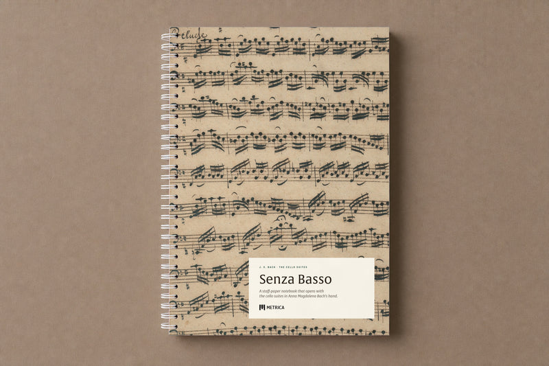 Senza Basso — the notebook closed: the Prelude of the first suite in Anna Magdalena Bach's hand on the cover, white spiral on the left, digitally composed product view