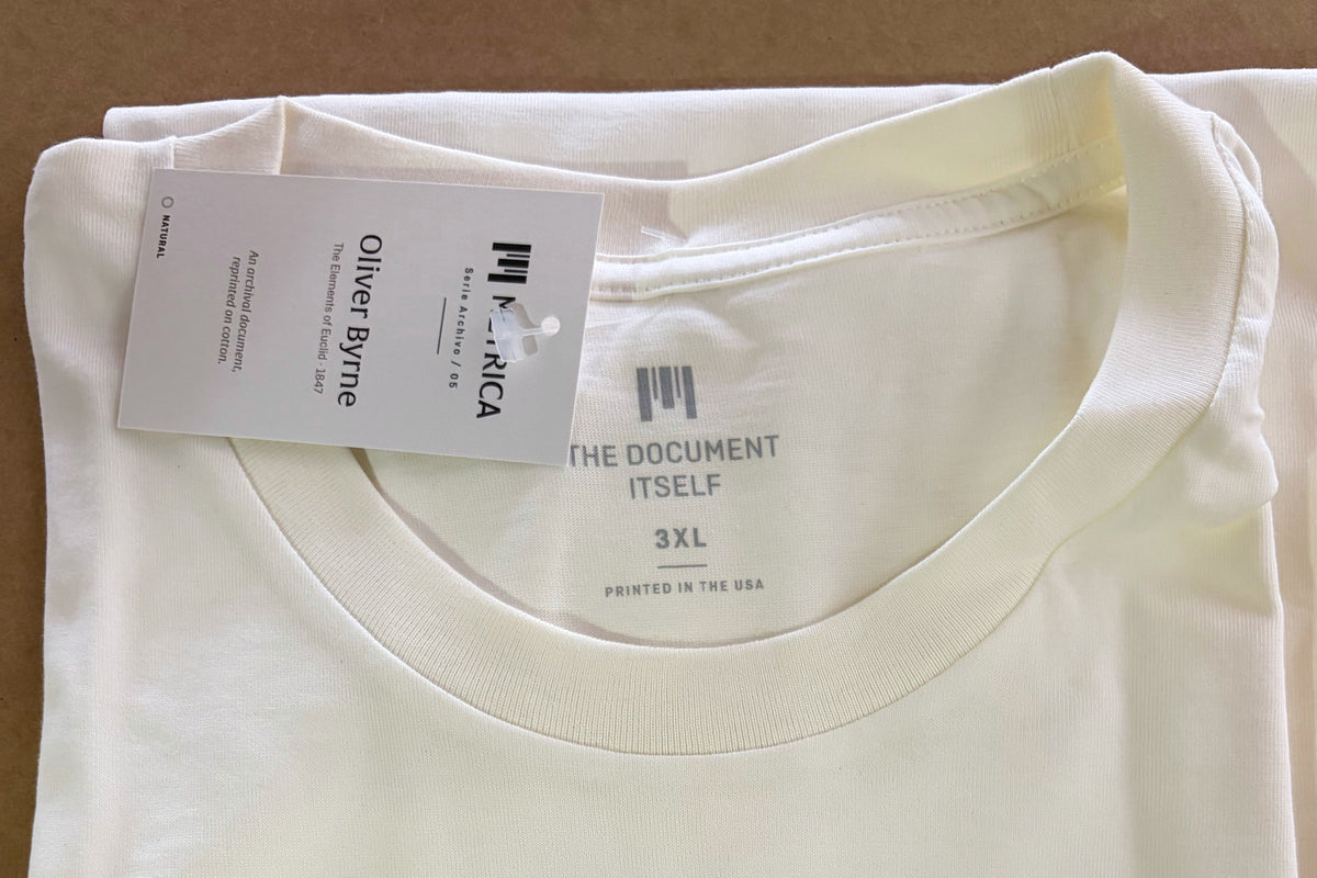 Close-up of the actual Oliver Byrne T-shirt: collar stitching, printed neck label and Métrica Serie Archivo hang tag.