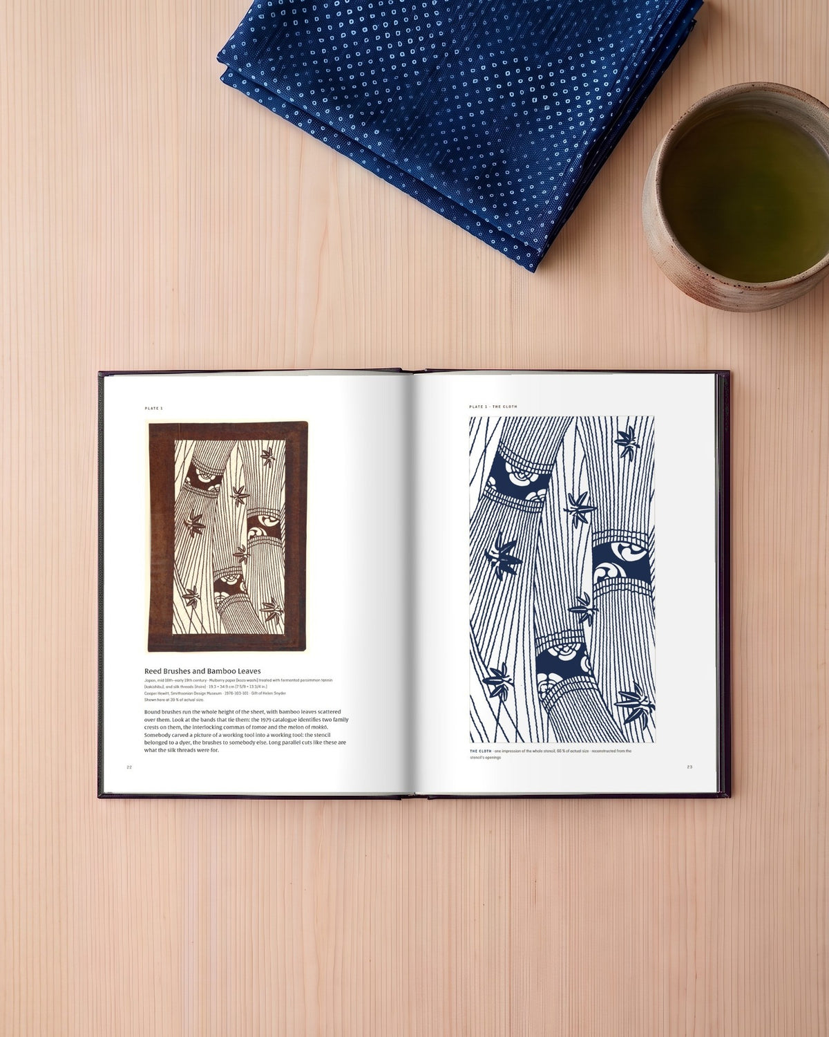 Katagami — Her Name Is on Every One of Them — the book open on a pale wooden table, at Plate 1: the stencil facing its cloth (digitally composed view with the actual printed pages)